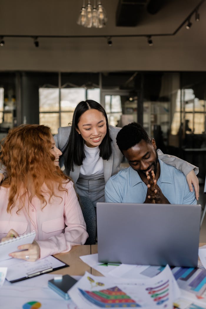 A diverse group of adults collaborating on a project in a modern office, using a laptop and documents.